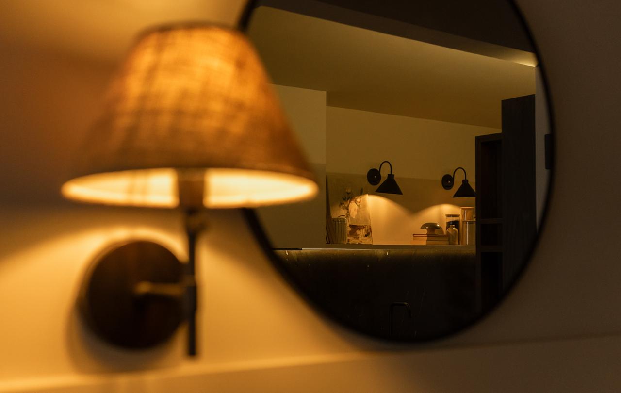Warm woven sconce light beside a round black-framed mirror in a styled DAZ Living interior